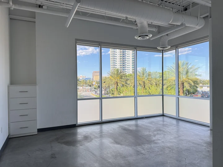 Empty corner room with tall windows overlooking palms and downtown buildings